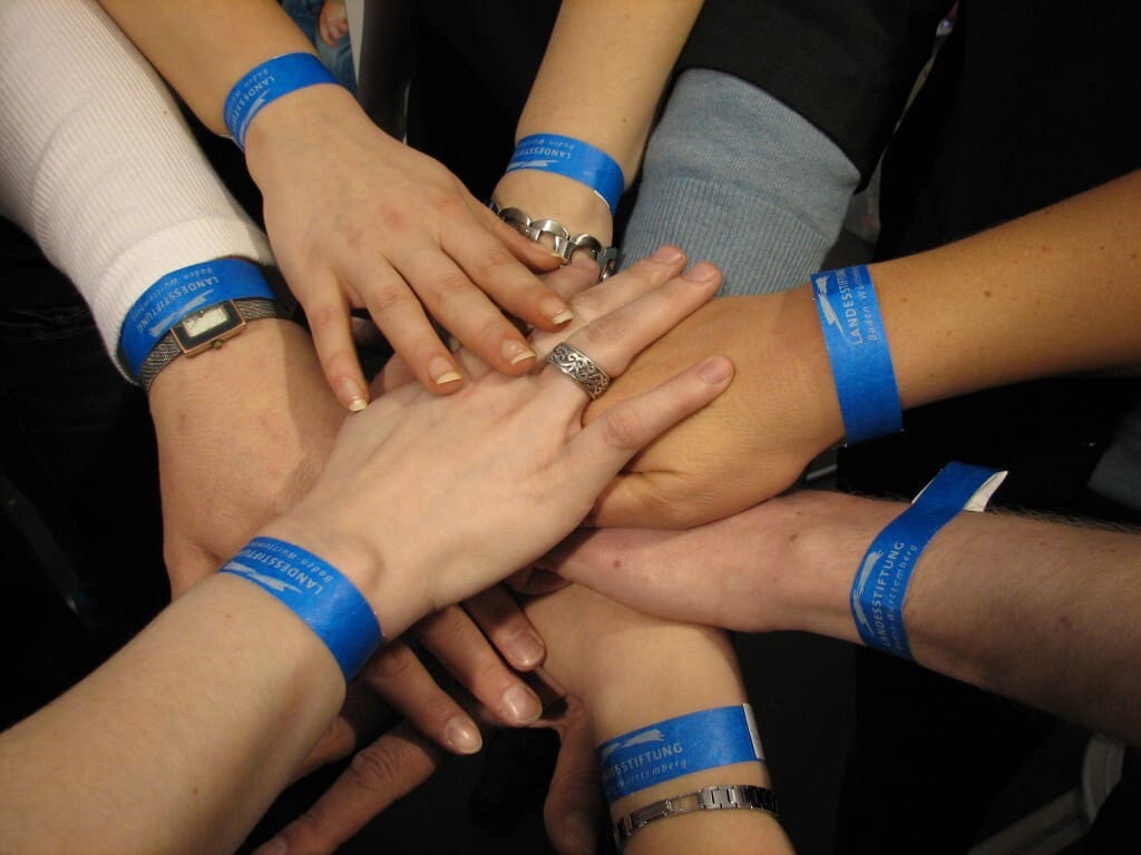 Sieben hellfarbene Hände mit blauen Armbändern legen ihre Hände im Kreis aufeinander. Dieses Bild findet man auf der Webseite vom Bundesverband Burnout und Depression.