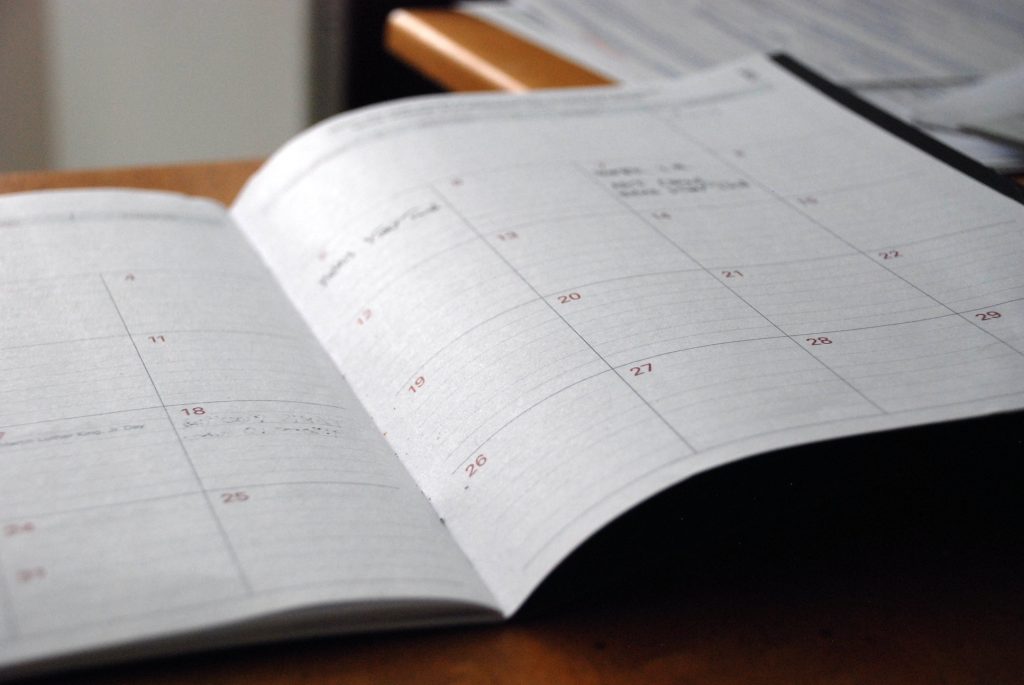 Ein offenes Buch mit Kalender Kästchen auf einem Holztisch. Dieses Bild findet man auf der Webseite vom Bundesverband Burnout und Depression.
